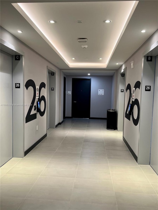 hall with light tile patterned flooring, a raised ceiling, and elevator