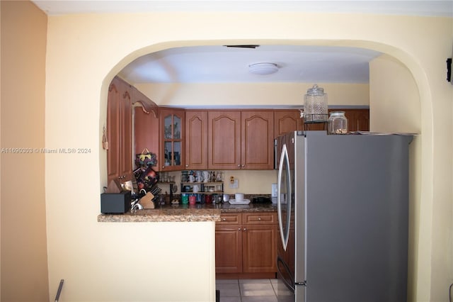 kitchen featuring stainless steel refrigerator, dark stone countertops, and light tile patterned flooring