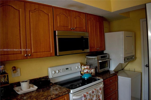 kitchen with dark stone counters, stacked washer and clothes dryer, and white electric stove