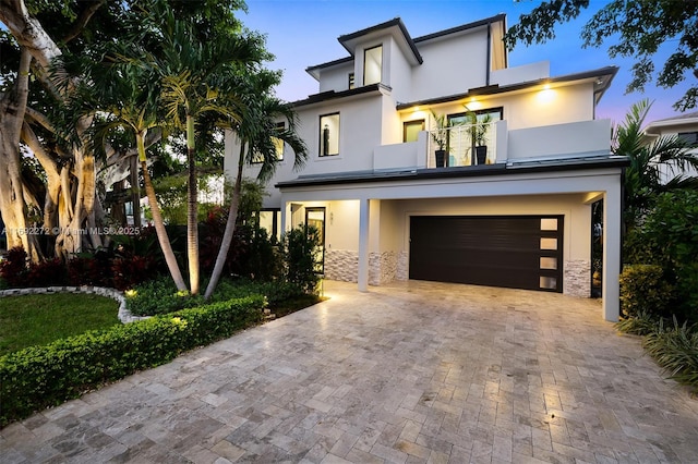 contemporary home featuring decorative driveway, a balcony, an attached garage, and stucco siding