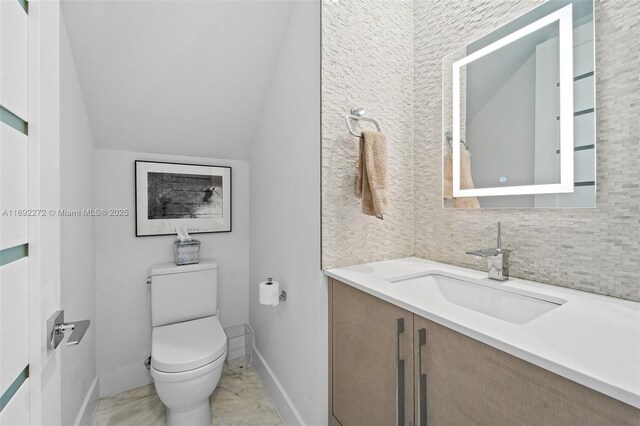 bathroom featuring vaulted ceiling, vanity, toilet, and baseboards