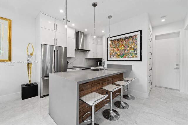 kitchen with high end refrigerator, white cabinets, wall chimney exhaust hood, modern cabinets, and a kitchen bar