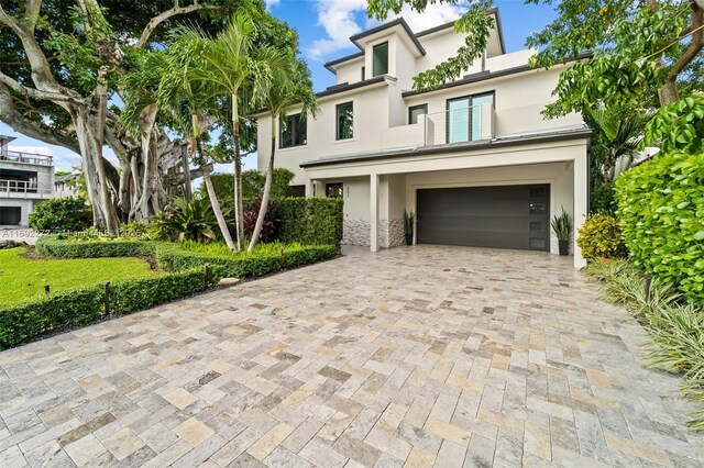 view of front facade featuring a garage, decorative driveway, a balcony, and stucco siding