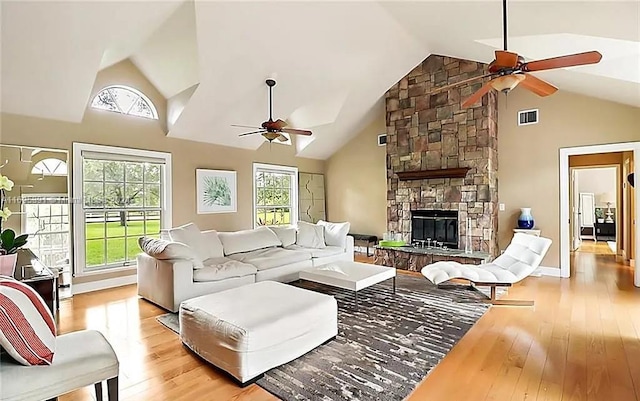 living room with ceiling fan, a stone fireplace, high vaulted ceiling, and light hardwood / wood-style flooring