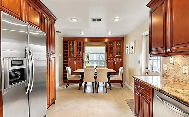 kitchen featuring backsplash, light stone countertops, light tile patterned flooring, and stainless steel appliances