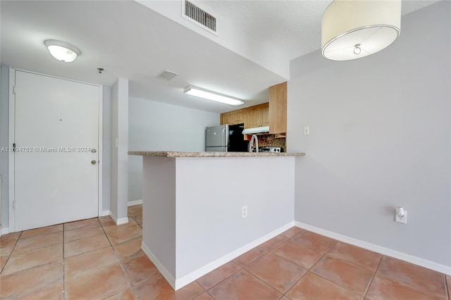 kitchen with kitchen peninsula, stainless steel fridge, sink, light brown cabinets, and light tile patterned flooring