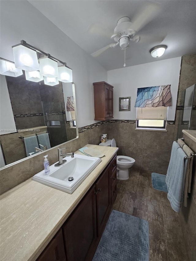 bathroom with hardwood / wood-style floors, tile walls, vanity, ceiling fan, and toilet