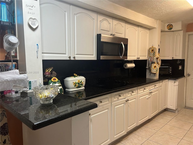 kitchen with dark stone counters, light tile patterned floors, a textured ceiling, black cooktop, and white cabinetry