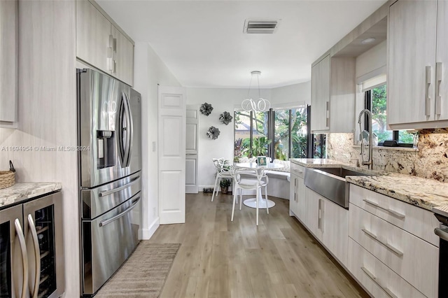 kitchen with sink, beverage cooler, light hardwood / wood-style flooring, stainless steel refrigerator with ice dispenser, and pendant lighting