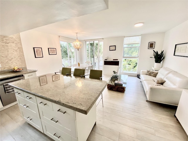 kitchen featuring a center island, light hardwood / wood-style flooring, decorative light fixtures, a kitchen bar, and white cabinetry