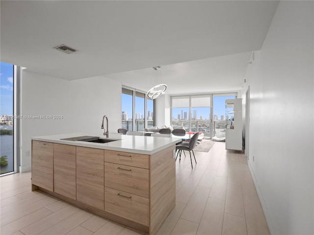 kitchen with sink, an island with sink, a chandelier, and a wall of windows