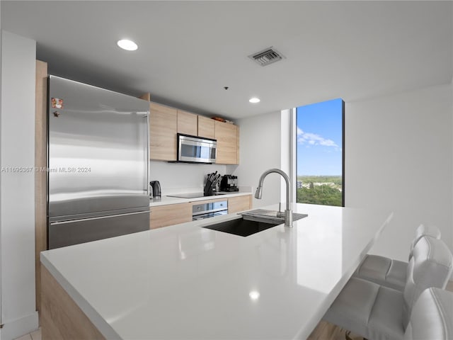 kitchen featuring appliances with stainless steel finishes, a kitchen breakfast bar, a kitchen island with sink, sink, and light brown cabinets