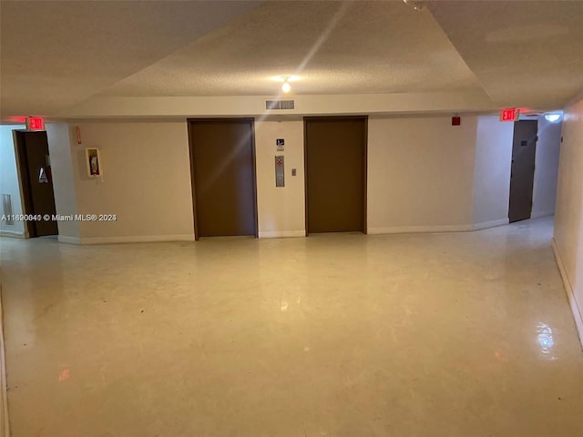 interior space featuring concrete flooring, a textured ceiling, and elevator