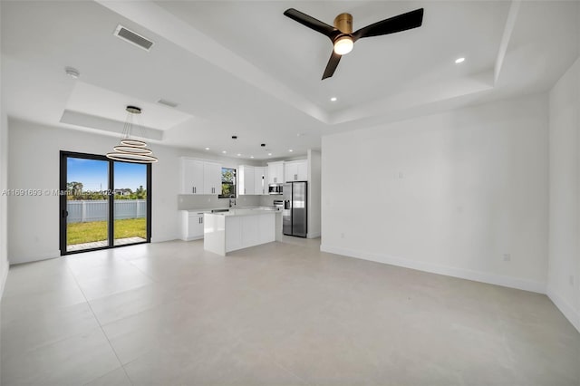 unfurnished living room featuring ceiling fan and a raised ceiling