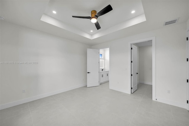 unfurnished bedroom featuring connected bathroom, ceiling fan, and a tray ceiling