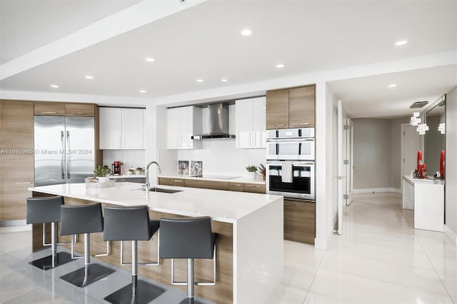 kitchen featuring white cabinetry, sink, wall chimney range hood, a kitchen breakfast bar, and a spacious island