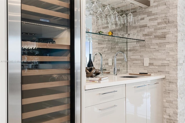 bar with backsplash, white cabinetry, sink, and beverage cooler