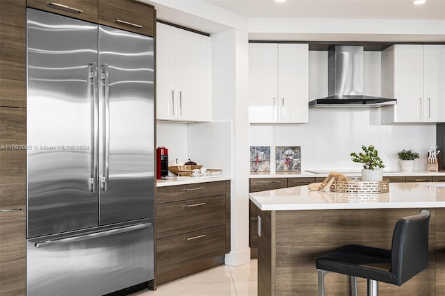 kitchen featuring white cabinets, dark brown cabinetry, wall chimney exhaust hood, and built in fridge