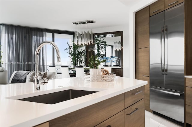 kitchen with pendant lighting, stainless steel built in refrigerator, sink, light tile patterned flooring, and dark brown cabinetry