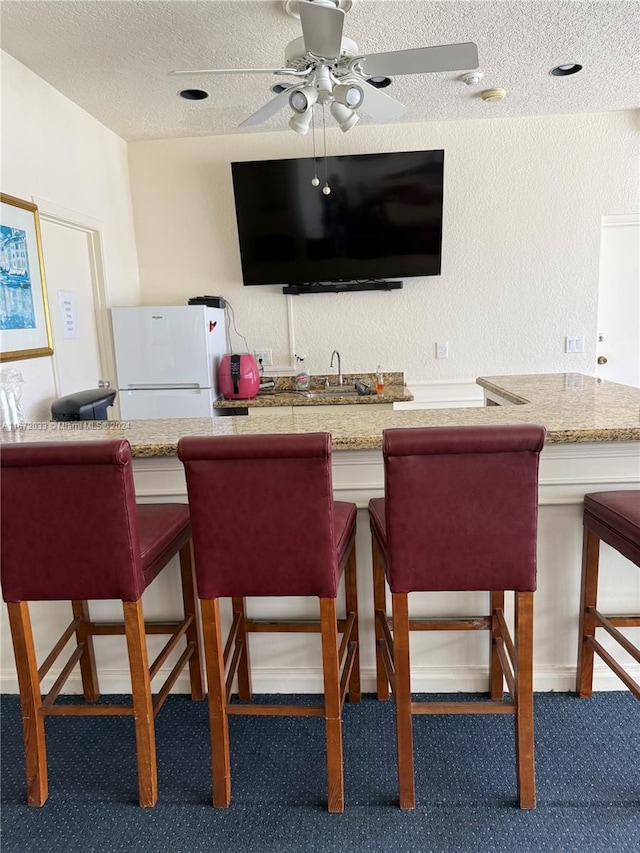 bar featuring ceiling fan, white fridge, sink, and a textured ceiling