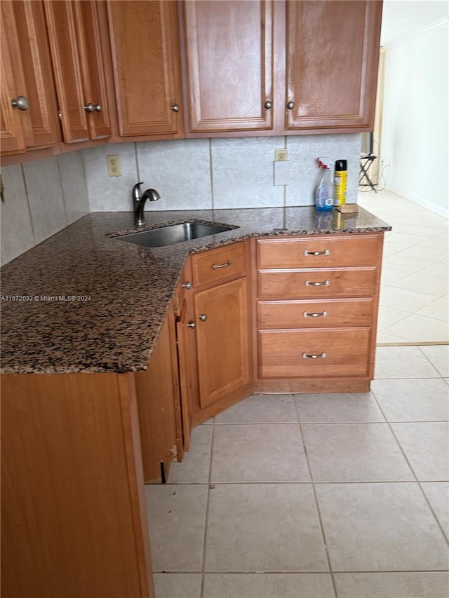 kitchen featuring light tile patterned flooring, tasteful backsplash, dark stone counters, and sink