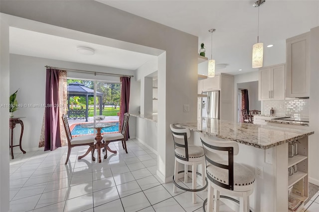 kitchen with decorative light fixtures, stainless steel fridge, white cabinetry, and light tile patterned floors