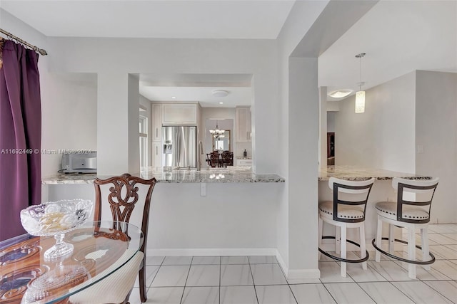 kitchen with light stone counters, stainless steel refrigerator with ice dispenser, kitchen peninsula, decorative light fixtures, and light tile patterned flooring