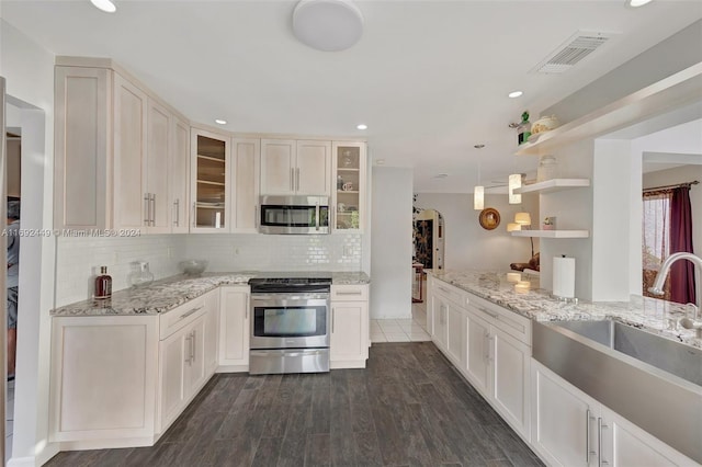 kitchen with backsplash, dark wood-type flooring, sink, light stone countertops, and appliances with stainless steel finishes