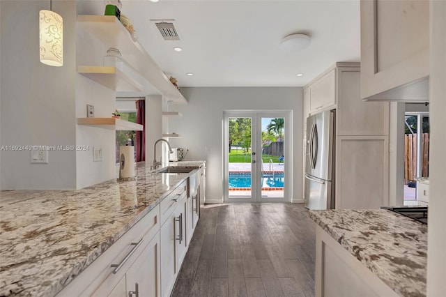 kitchen featuring light stone countertops, stainless steel fridge, dark hardwood / wood-style flooring, and hanging light fixtures