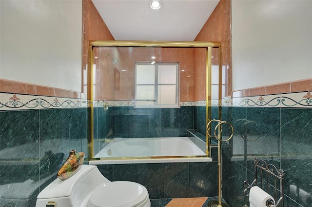 bathroom with toilet, bath / shower combo with glass door, and tile walls