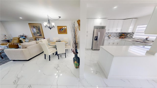 kitchen featuring sink, hanging light fixtures, backsplash, stainless steel fridge, and white cabinets