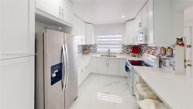 kitchen featuring white appliances, white cabinets, sink, decorative backsplash, and a breakfast bar area