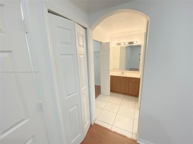 corridor with sink, light tile patterned floors, and ornamental molding