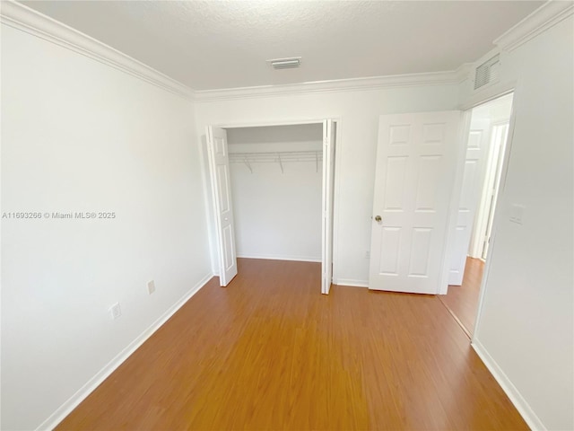 unfurnished bedroom featuring a closet, crown molding, a textured ceiling, and hardwood / wood-style floors