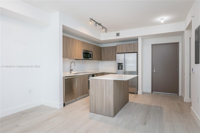 kitchen with sink, light hardwood / wood-style floors, track lighting, a kitchen island, and appliances with stainless steel finishes