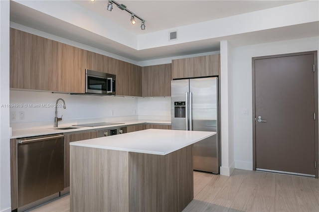 kitchen with rail lighting, stainless steel appliances, sink, light hardwood / wood-style flooring, and a center island