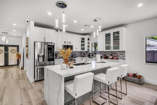 kitchen with light hardwood / wood-style floors, stainless steel fridge, white cabinetry, and an island with sink