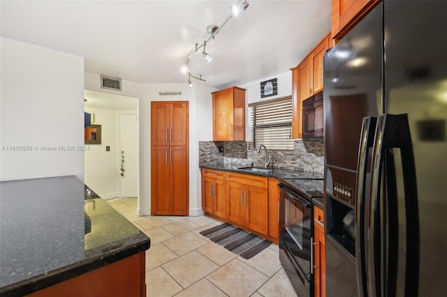 kitchen with sink, tasteful backsplash, dark stone countertops, light tile patterned flooring, and black appliances