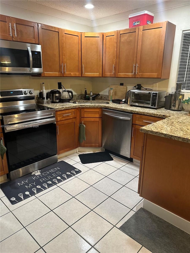 kitchen with sink, stainless steel appliances, light stone counters, a textured ceiling, and light tile patterned floors