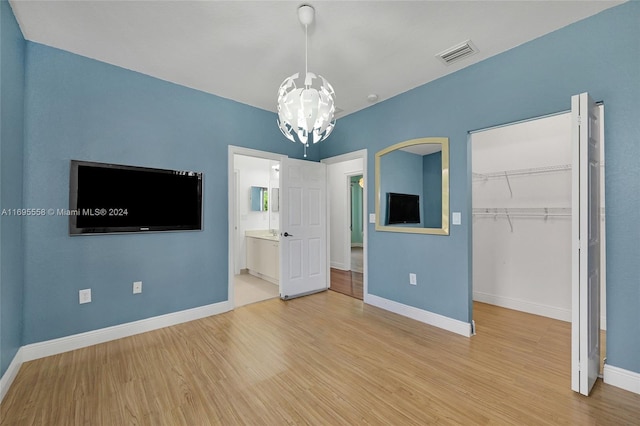 unfurnished bedroom with ensuite bathroom, a closet, an inviting chandelier, and light wood-type flooring