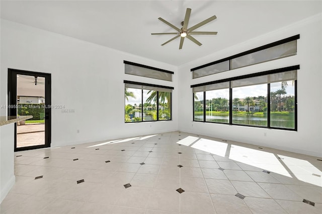 spare room with a water view, ceiling fan, a healthy amount of sunlight, and light tile patterned flooring