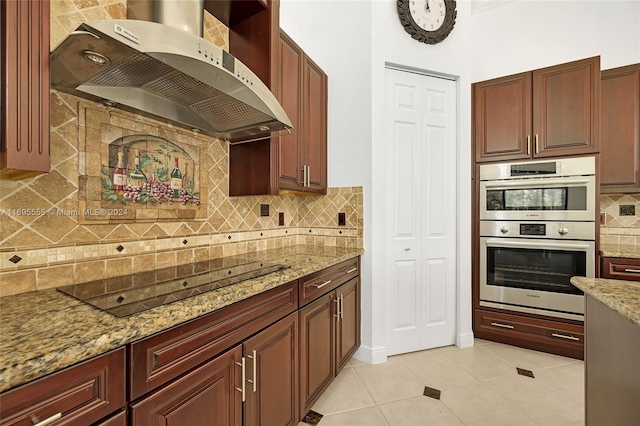 kitchen featuring light stone countertops, tasteful backsplash, wall chimney exhaust hood, stainless steel double oven, and black electric cooktop