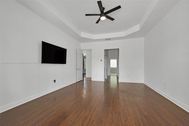 empty room featuring a raised ceiling, ceiling fan, and dark hardwood / wood-style flooring