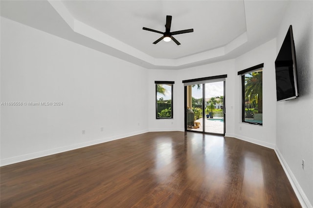 empty room with a tray ceiling, ceiling fan, and dark wood-type flooring