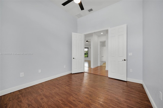 unfurnished bedroom with ceiling fan, a towering ceiling, and dark wood-type flooring