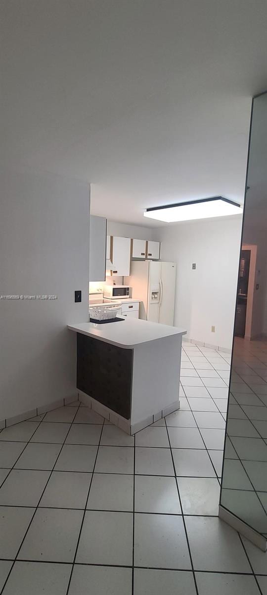 kitchen with kitchen peninsula, white appliances, white cabinets, and light tile patterned floors