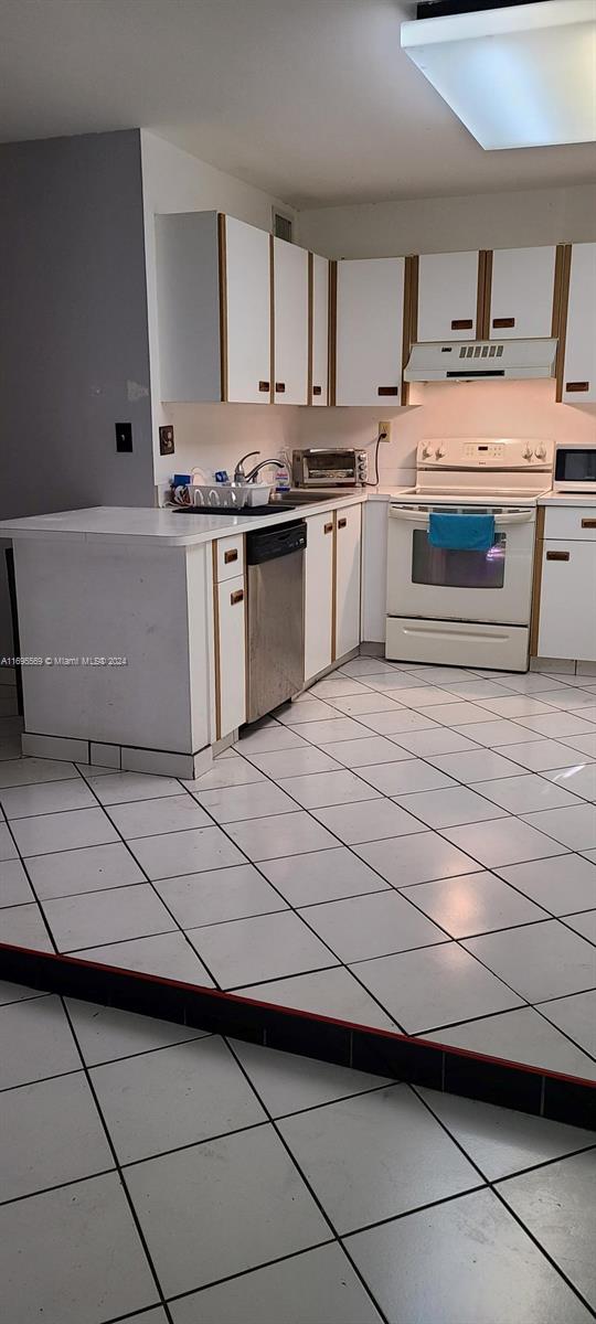 kitchen with white cabinets, white appliances, light tile patterned floors, and a skylight