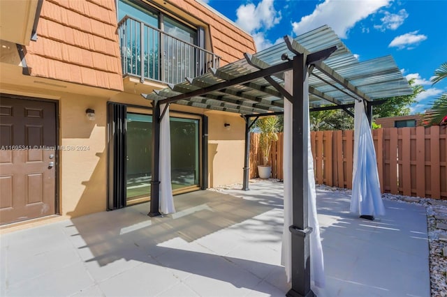 view of patio featuring a pergola and a balcony