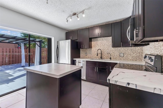 kitchen featuring sink, a center island, stainless steel appliances, light stone counters, and a textured ceiling