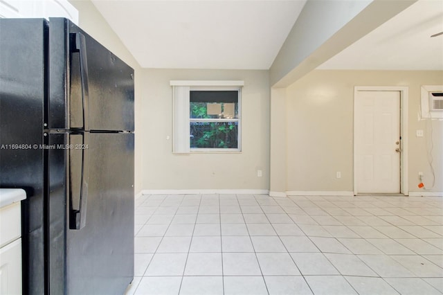 interior space featuring black refrigerator, a wall unit AC, lofted ceiling, and light tile patterned flooring